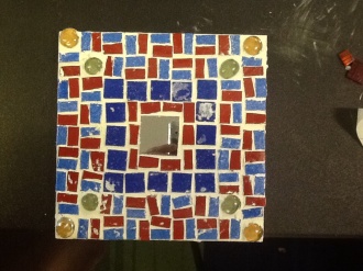 imageSquare tile with small square mirror in centre. Red and blue geometric pattern with green and yellow glass beads, two diagonally on each corner.