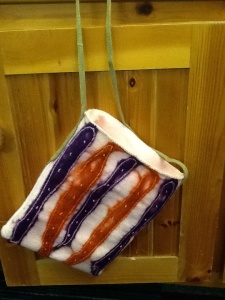 Cream base with blue and orange stripe felt square bag. Green cord straps. 