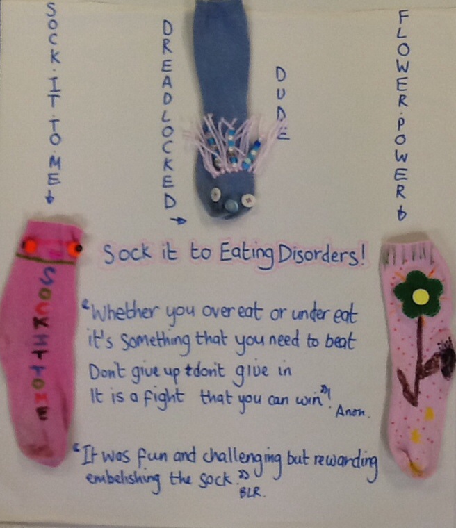 Sock it To Eating Disorders display. Tiltle written in the middle of the display in blue and pink marker. Two quotes underneath from members of  the group.  The socks have names written down the display above the two pink socks either side of the quotes. The blue sock is above the quotes in the centre of the display  with the name written either side of it. 