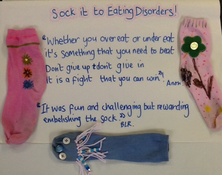 Sock it to Eating Disorders display. Writing in blue are two quotes from the members who decorated the socks. The pink socks are arranged either side and the blue sock is under the quotes.
