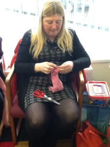 ATS craft member sewing two very small orange pom poms onto the top of her pink sock.